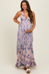 woman wearing a pink and blue floral maternity maxi dress with halter neck and ruffled hem, holding her baby bump