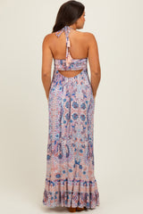 woman wearing a patterned halter neck maternity maxi dress with an open back and ruffled hem