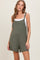 woman wearing an olive green sleeveless romper with a front pocket and a white tank top underneath