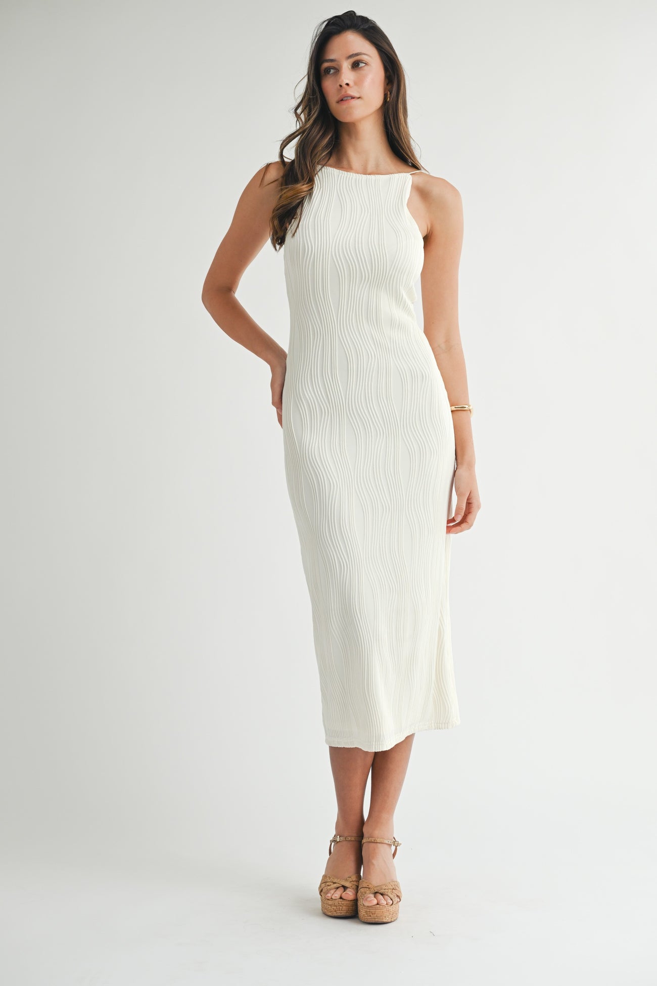 woman wearing a cream-colored ribbed midi dress with a halter neckline and a fitted silhouette