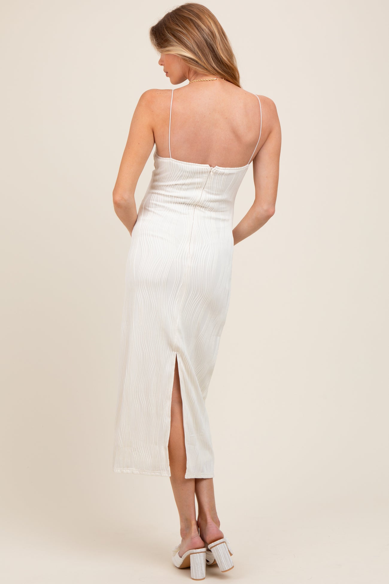 woman wearing a light beige maternity dress with a slit at the back and thin straps