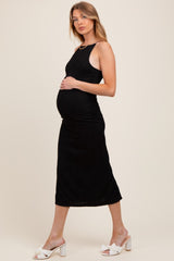woman wearing a black ribbed maternity dress and showing her baby bump, styled with white heeled slides