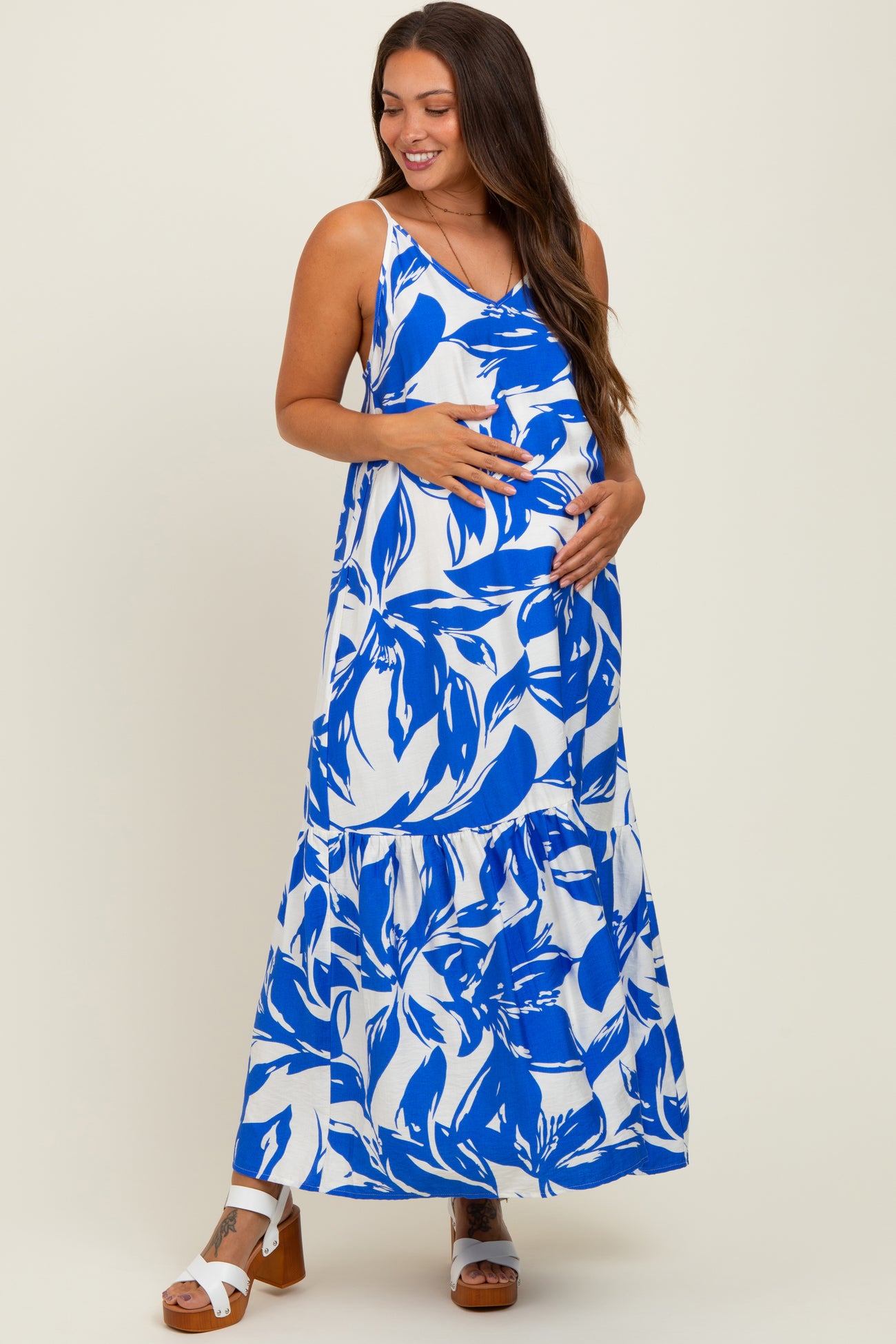woman wearing a blue and white floral print maternity maxi dress and holding her baby bump