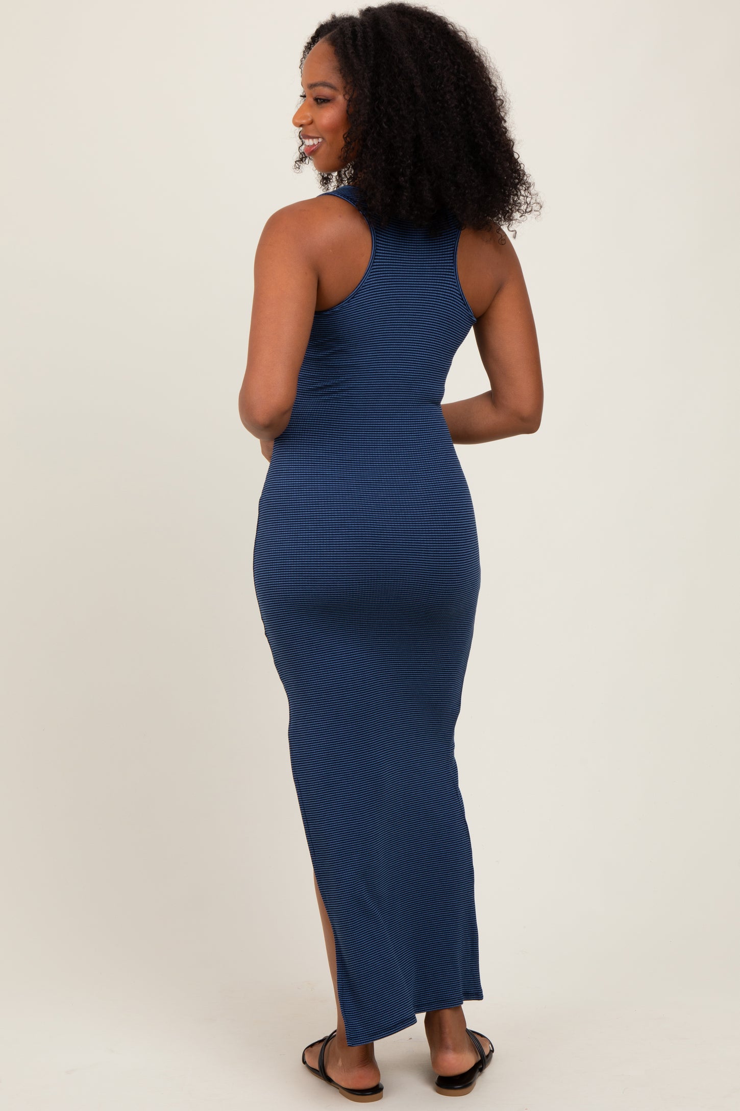 woman wearing a navy blue ribbed maxi dress with a fitted silhouette and a side slit, shown from the back