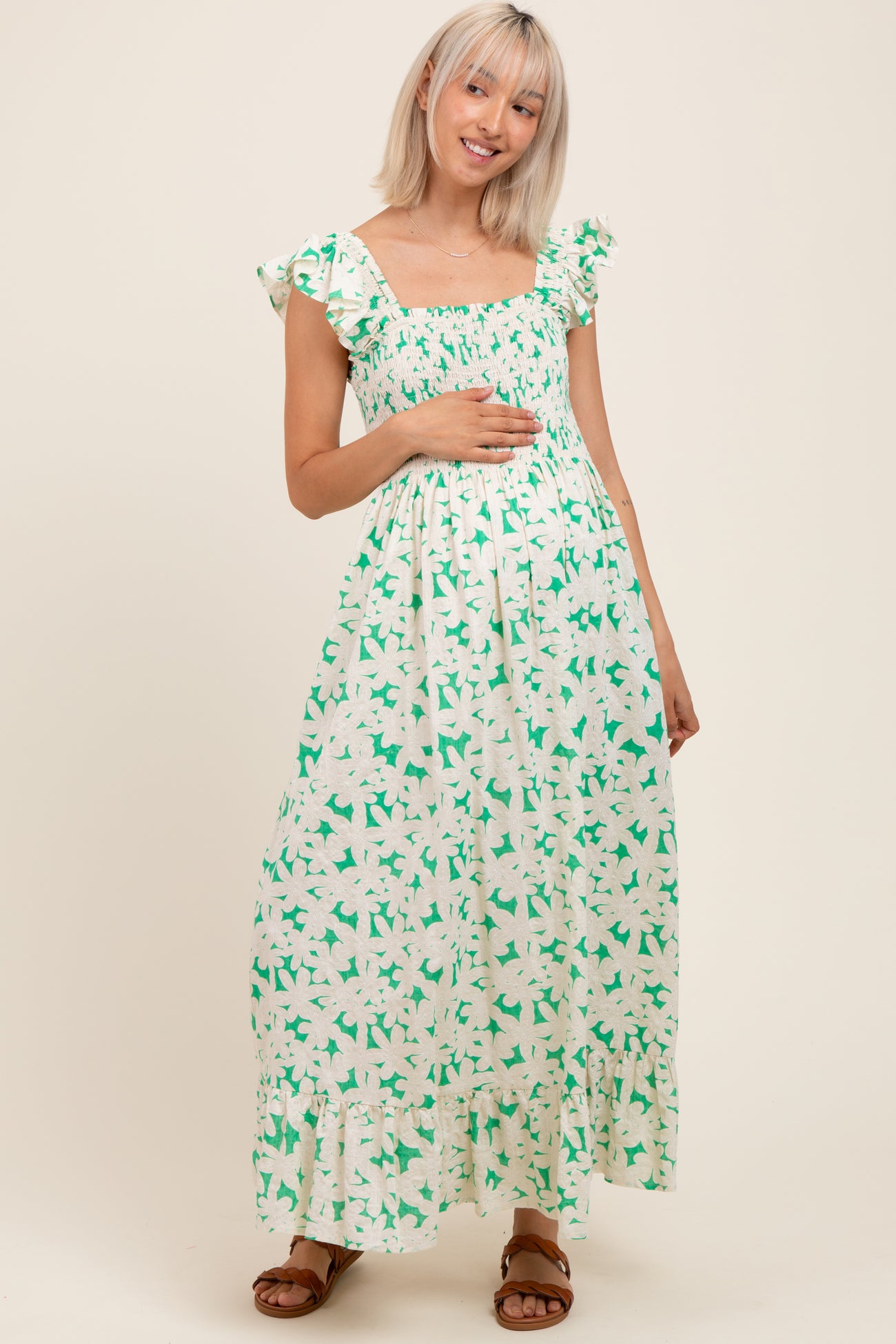 woman wearing a green and white floral maternity maxi dress with ruffled sleeves and holding her baby bump