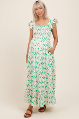 woman wearing a green and white floral maternity dress with smocked bodice and ruffled sleeves, holding her baby bump