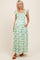 woman wearing a green and white floral maternity dress with smocked bodice and ruffled sleeves, holding her baby bump
