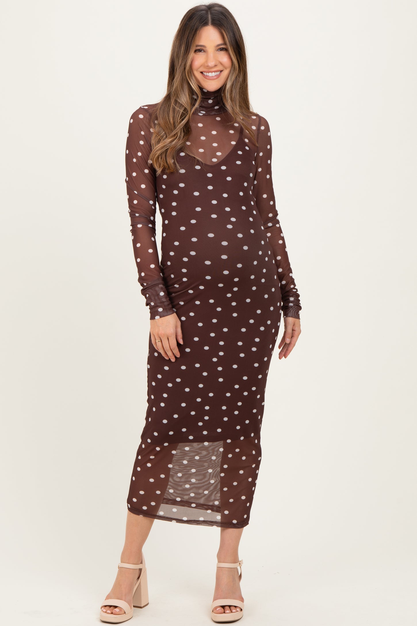 woman wearing a brown polka dot long sleeve maternity dress with a fitted silhouette and holding her baby bump
