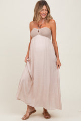 woman wearing a beige strapless maternity maxi dress with a smocked bodice and flowing skirt, showing her baby bump