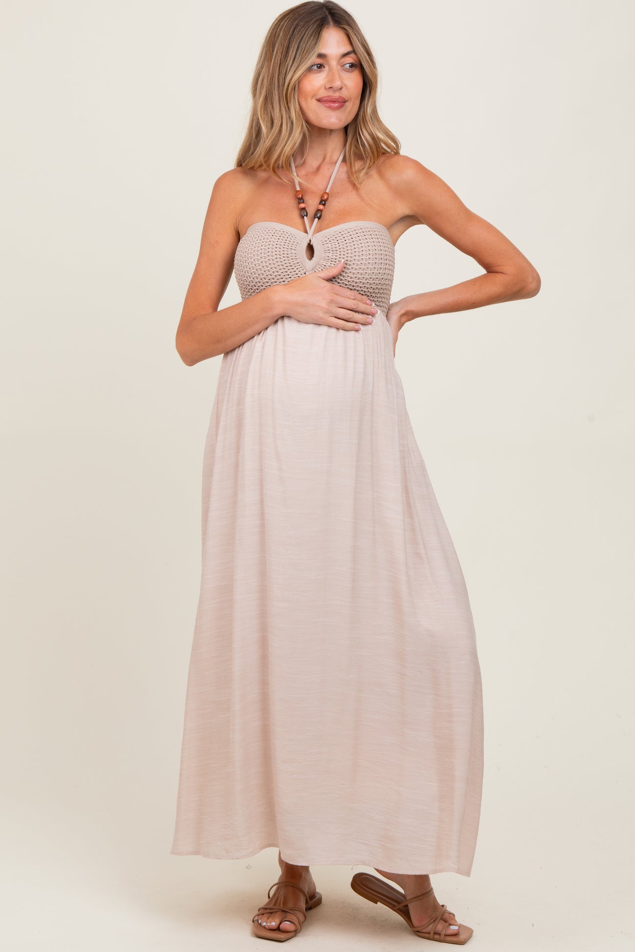 woman wearing a beige strapless maternity maxi dress holding her baby bump