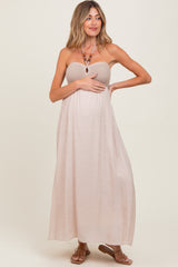 woman wearing a beige strapless maternity maxi dress holding her baby bump