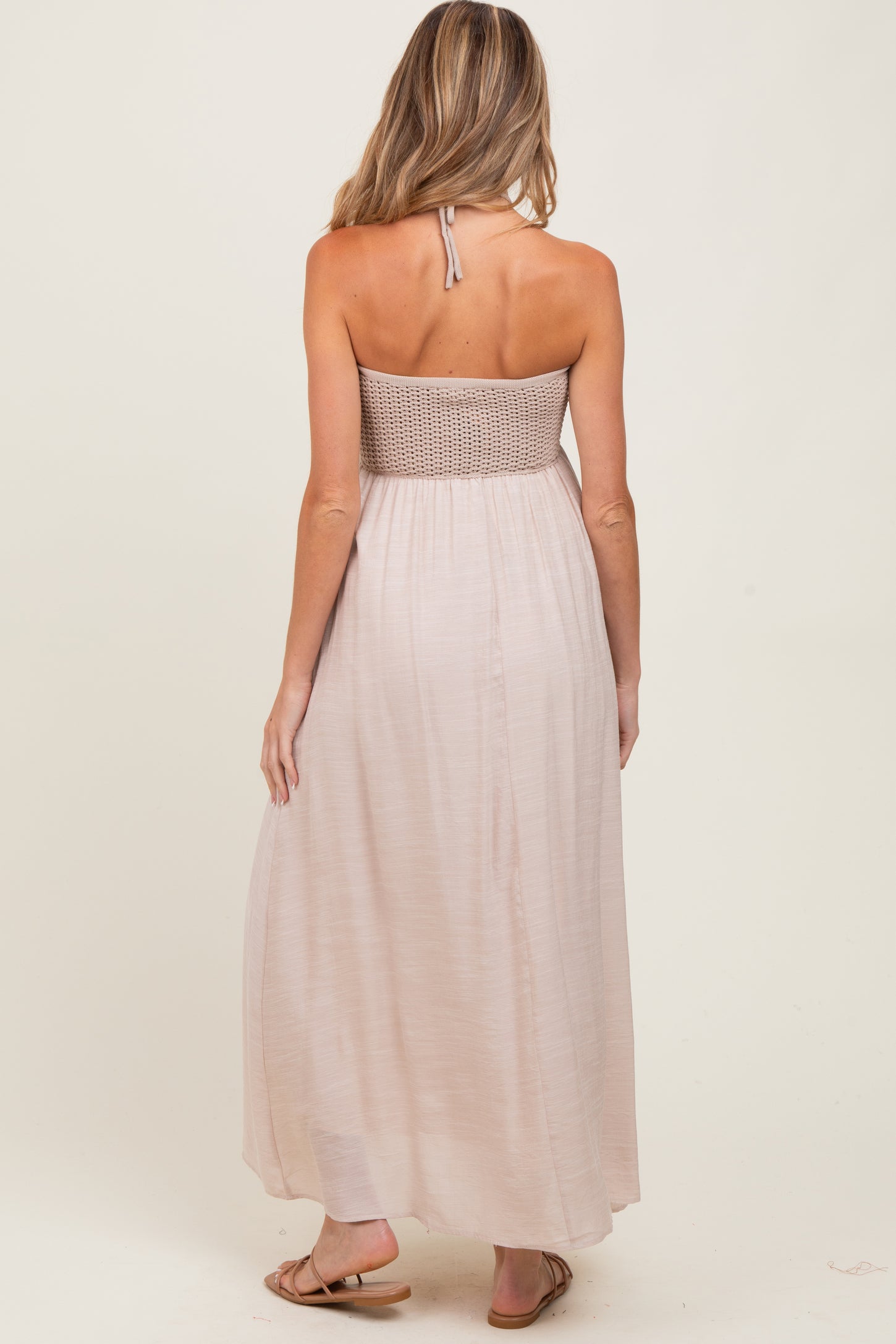 woman wearing a light pink maternity maxi dress with a smocked bodice and halter neck design