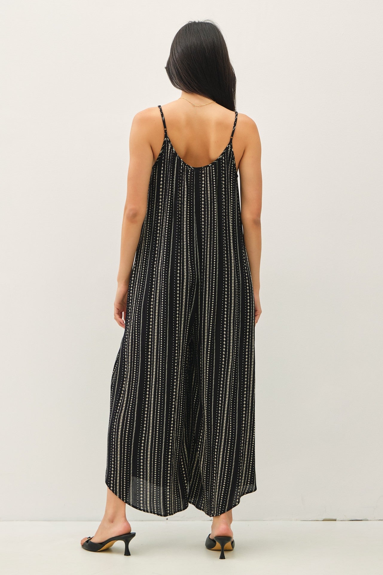 woman wearing a black and white striped jumpsuit with wide legs and spaghetti straps, viewed from the back