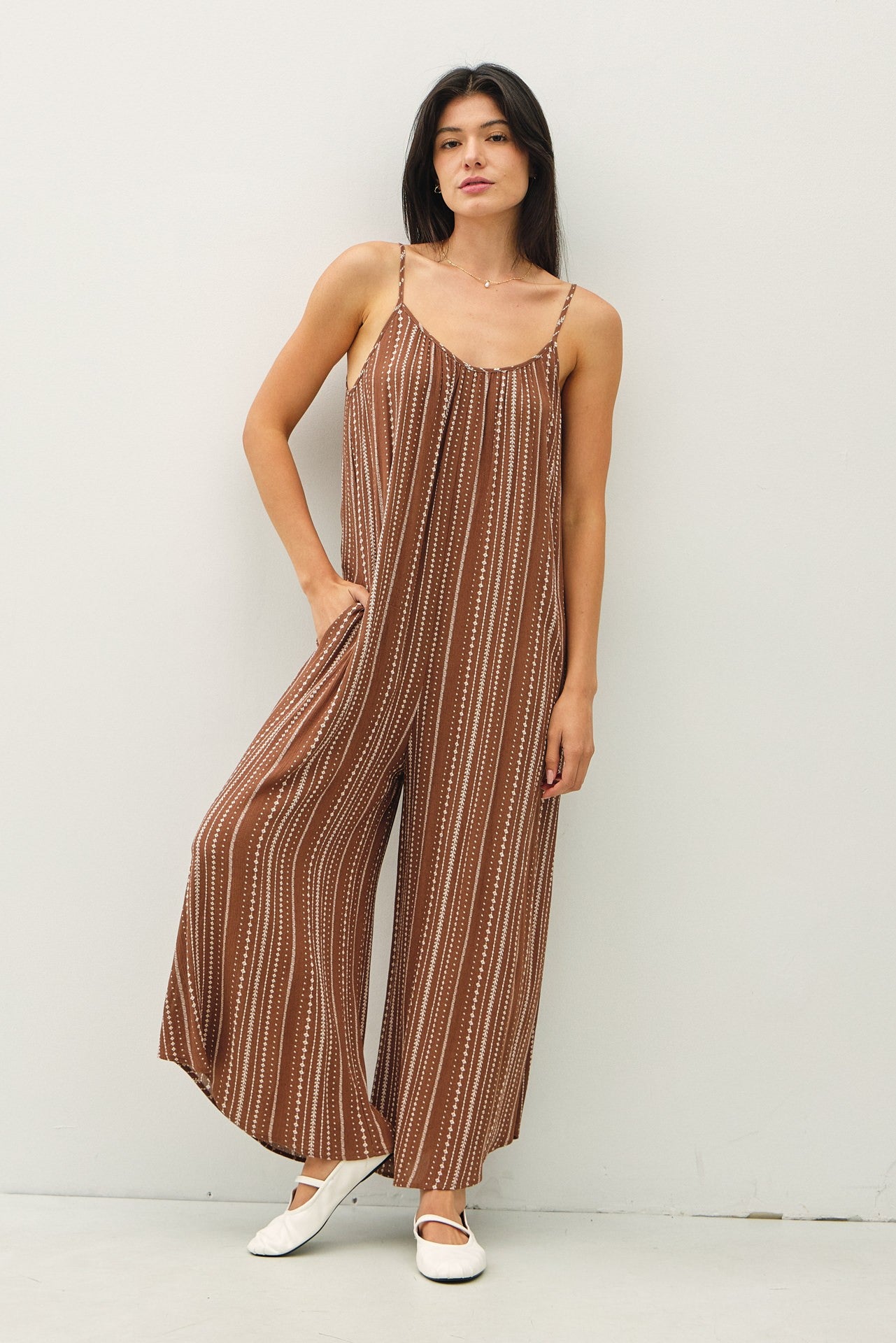woman wearing a brown striped spaghetti strap jumpsuit with wide legs and pockets