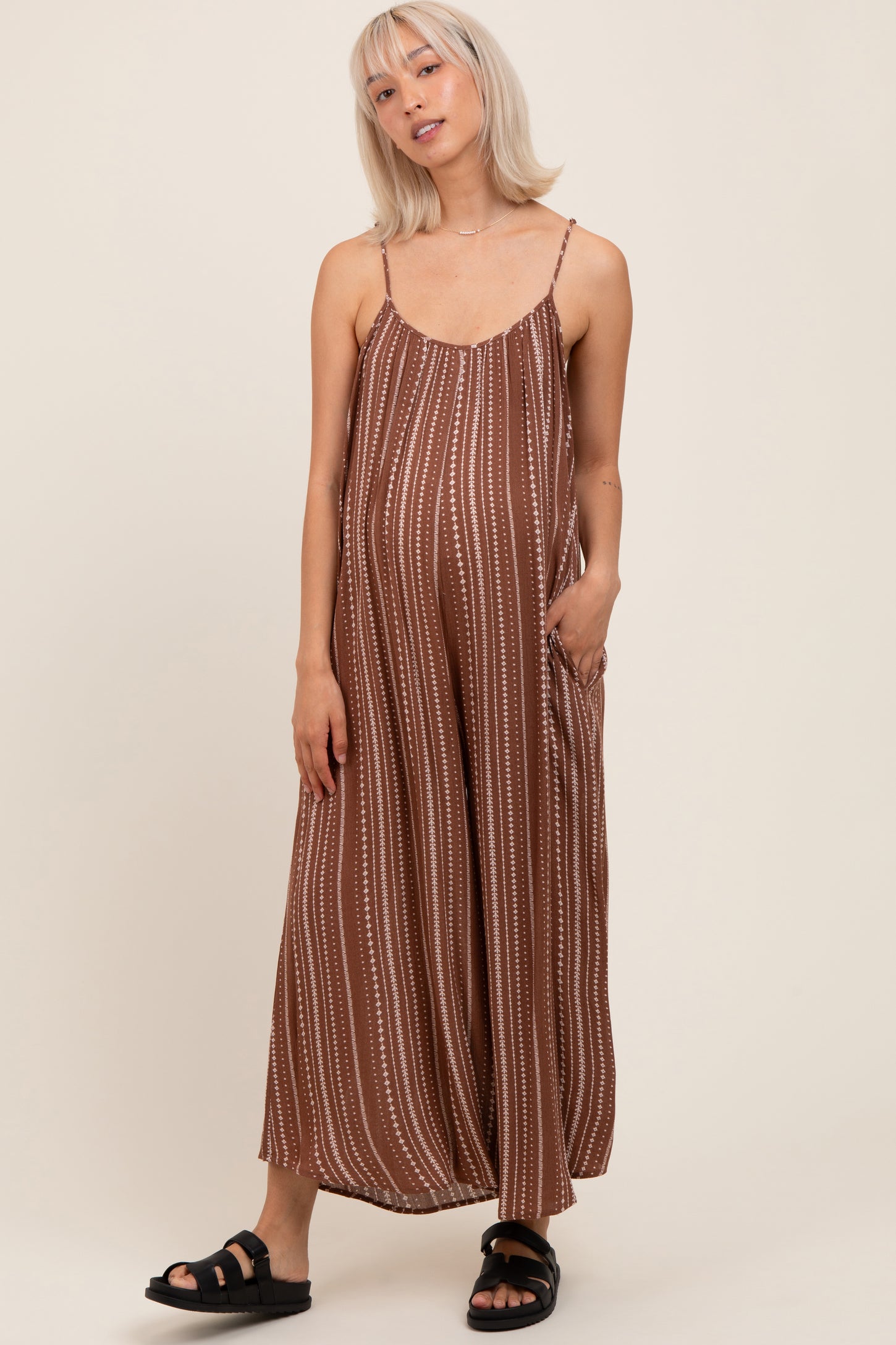 woman wearing a brown striped maternity maxi dress with adjustable straps and pockets, showing her baby bump