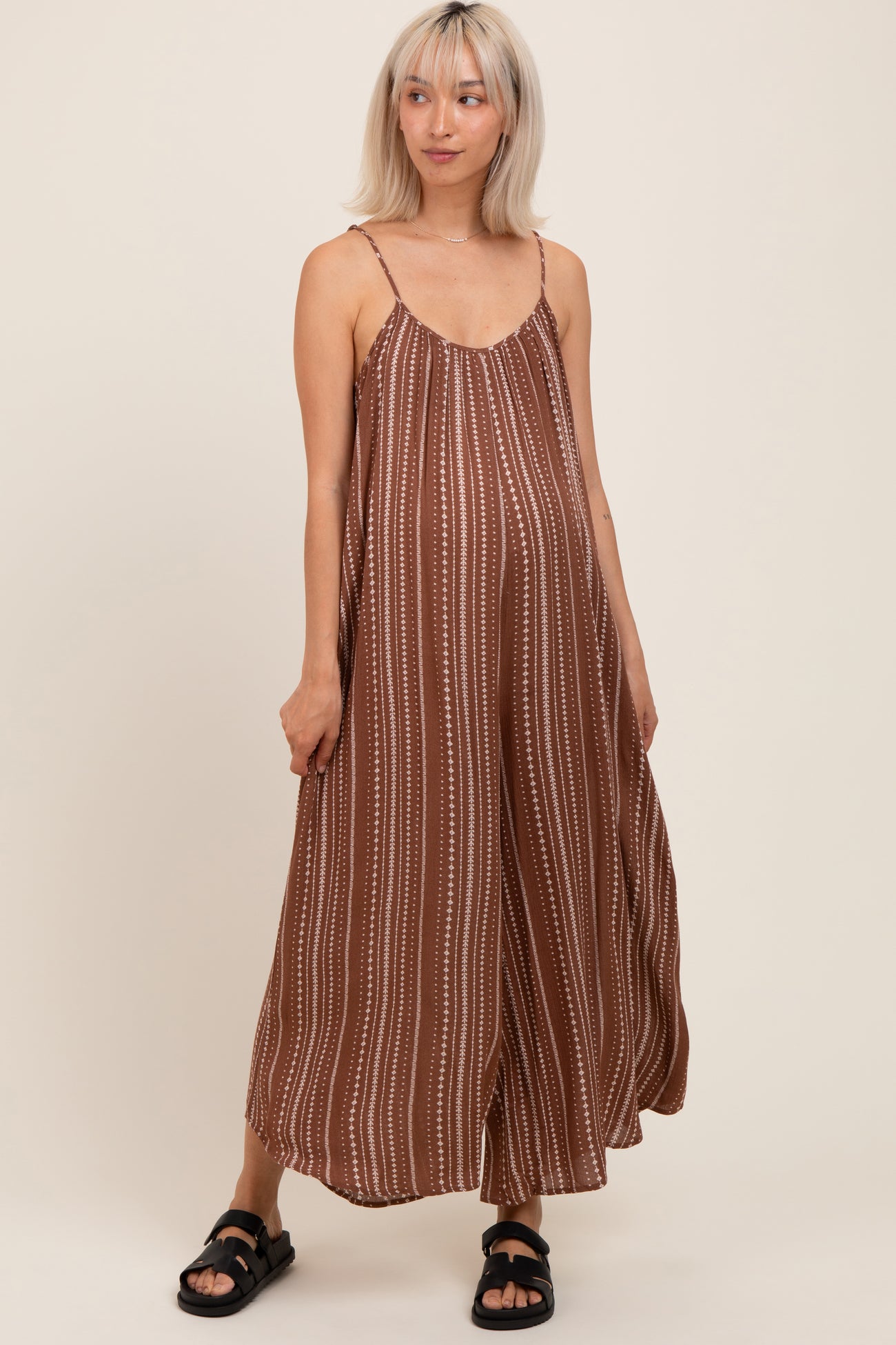 woman wearing a brown striped maternity dress with spaghetti straps and a relaxed fit, holding her baby bump