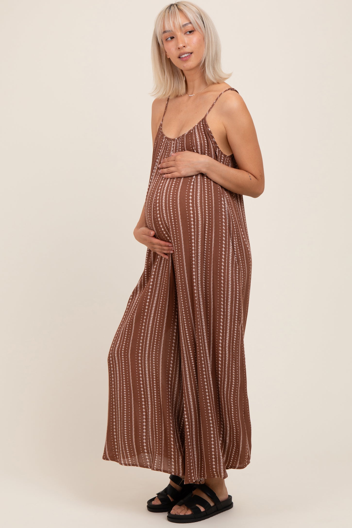 woman wearing a brown striped maternity jumpsuit and holding her baby bump
