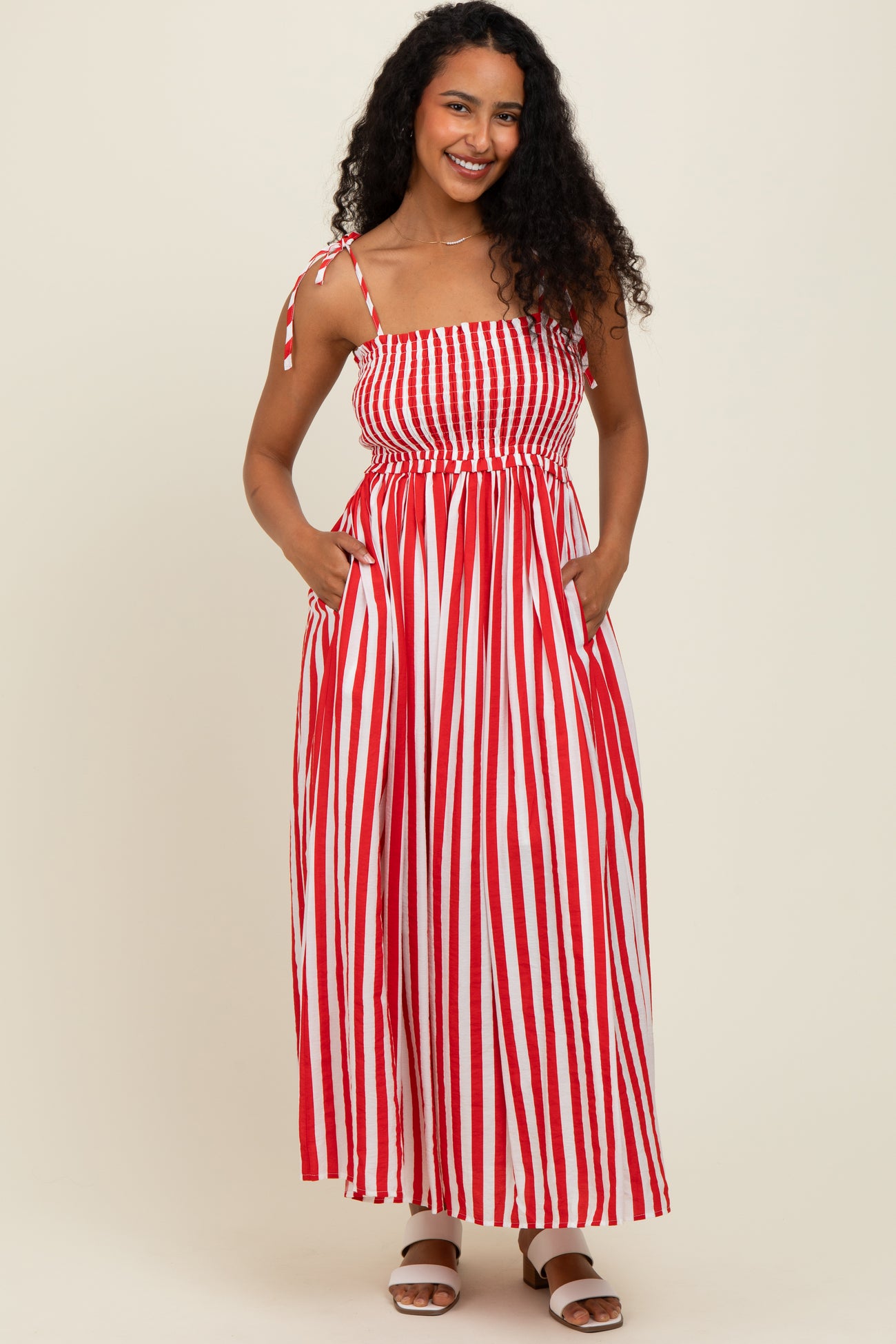woman wearing a red and white striped maxi dress with a smocked bodice and adjustable straps, posing with pockets