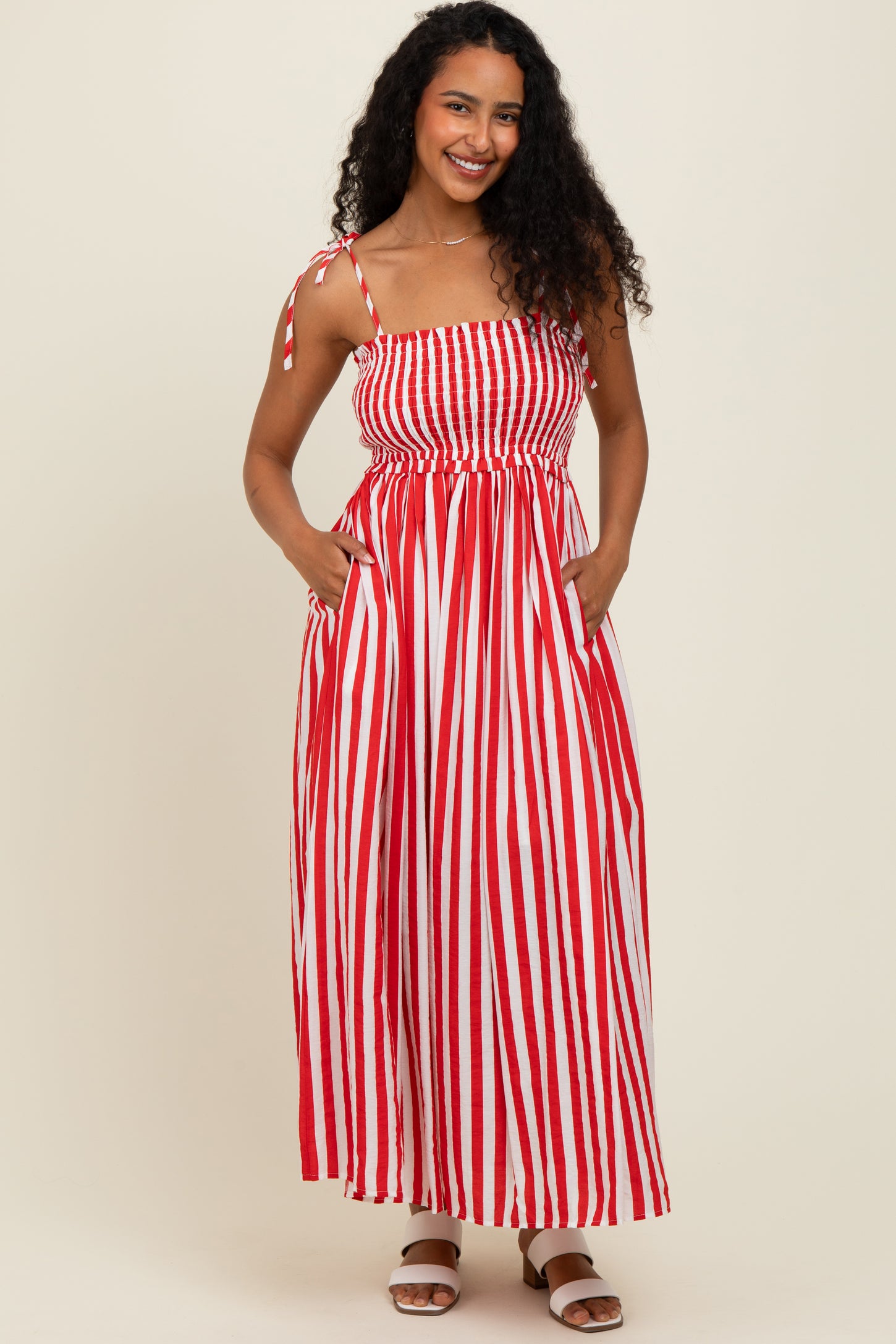 woman wearing a red and white striped maxi dress with a smocked bodice and adjustable straps, posing with pockets