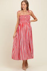 woman wearing a red and white striped maternity dress with tie shoulder straps and a smocked bodice, showing her baby bump