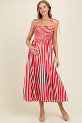woman wearing a red and white striped maternity dress with tie straps, gently holding her baby bump