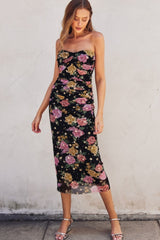 woman wearing a black floral strapless midi dress with ruching and side slit, styled with silver heels