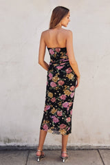 woman wearing a black floral strapless midi dress with a fitted silhouette and a slit at the back
