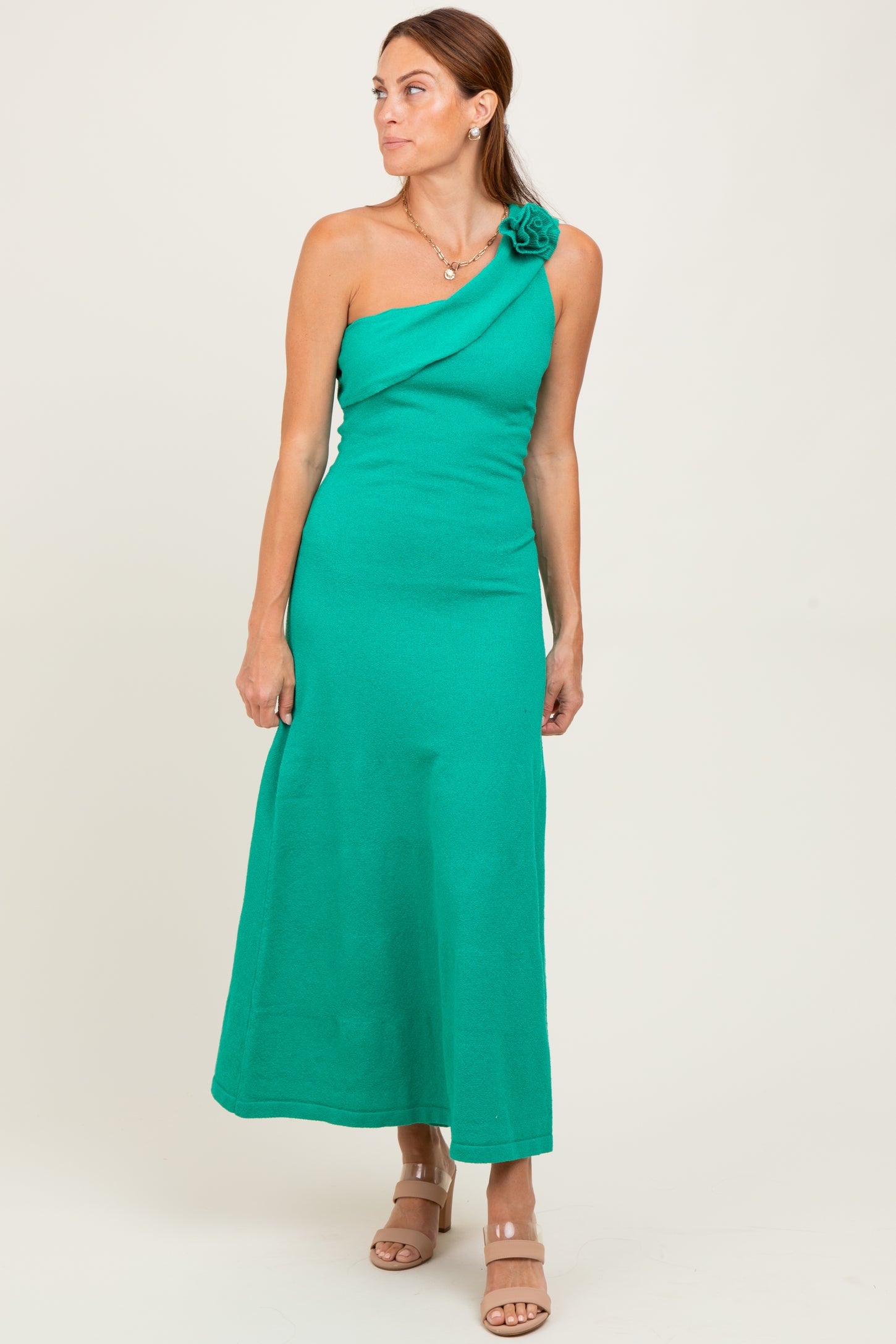 woman wearing a green one-shoulder maxi dress with a flower detail on the shoulder, standing confidently