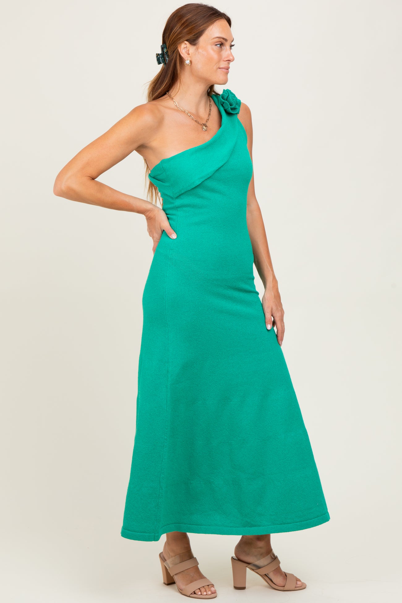 woman wearing a green one-shoulder maxi dress with a floral accent, styled with a hair clip and heels