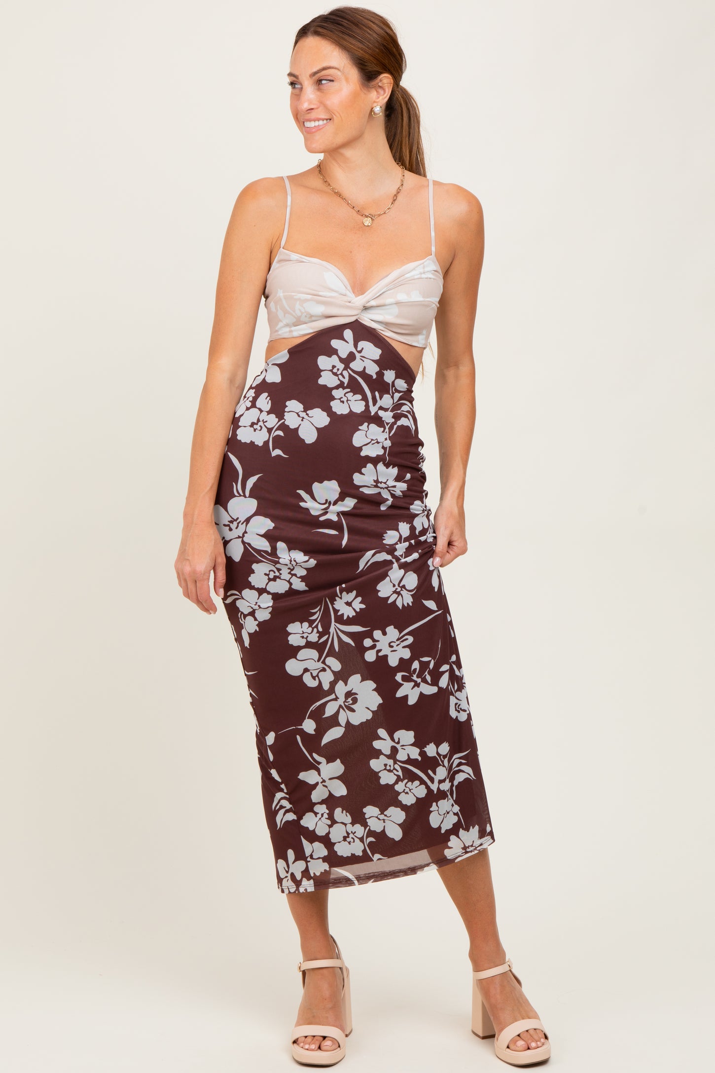 woman wearing a brown floral midi dress with a fitted silhouette and spaghetti straps, standing with one hand on her hip