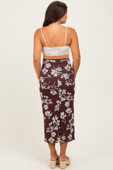 woman wearing a brown floral maternity skirt and a white cropped top, showing her back and a visible baby bump