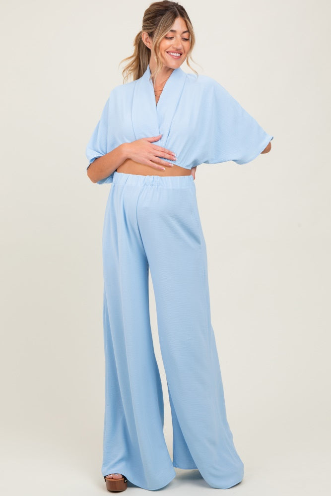 woman wearing a light blue maternity two-piece set with wide-leg pants and a cropped top, displaying her baby bump
