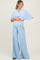 woman wearing a light blue maternity two-piece set with wide-leg pants and a cropped top, displaying her baby bump