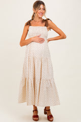 woman wearing a beige polka dot maternity maxi dress with tie straps and holding her baby bump