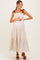 woman wearing a beige polka dot maternity maxi dress with tie straps and holding her baby bump