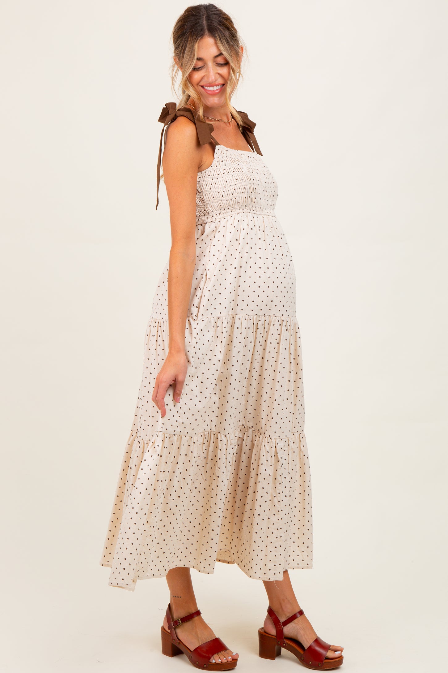 woman wearing a beige polka dot maternity dress with smocked bodice and tie shoulder straps, showcasing her baby bump