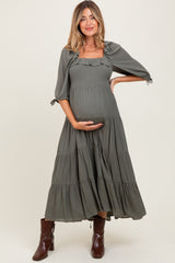 woman wearing a sage green maternity dress with puff sleeves and tiered skirt, holding her baby bump