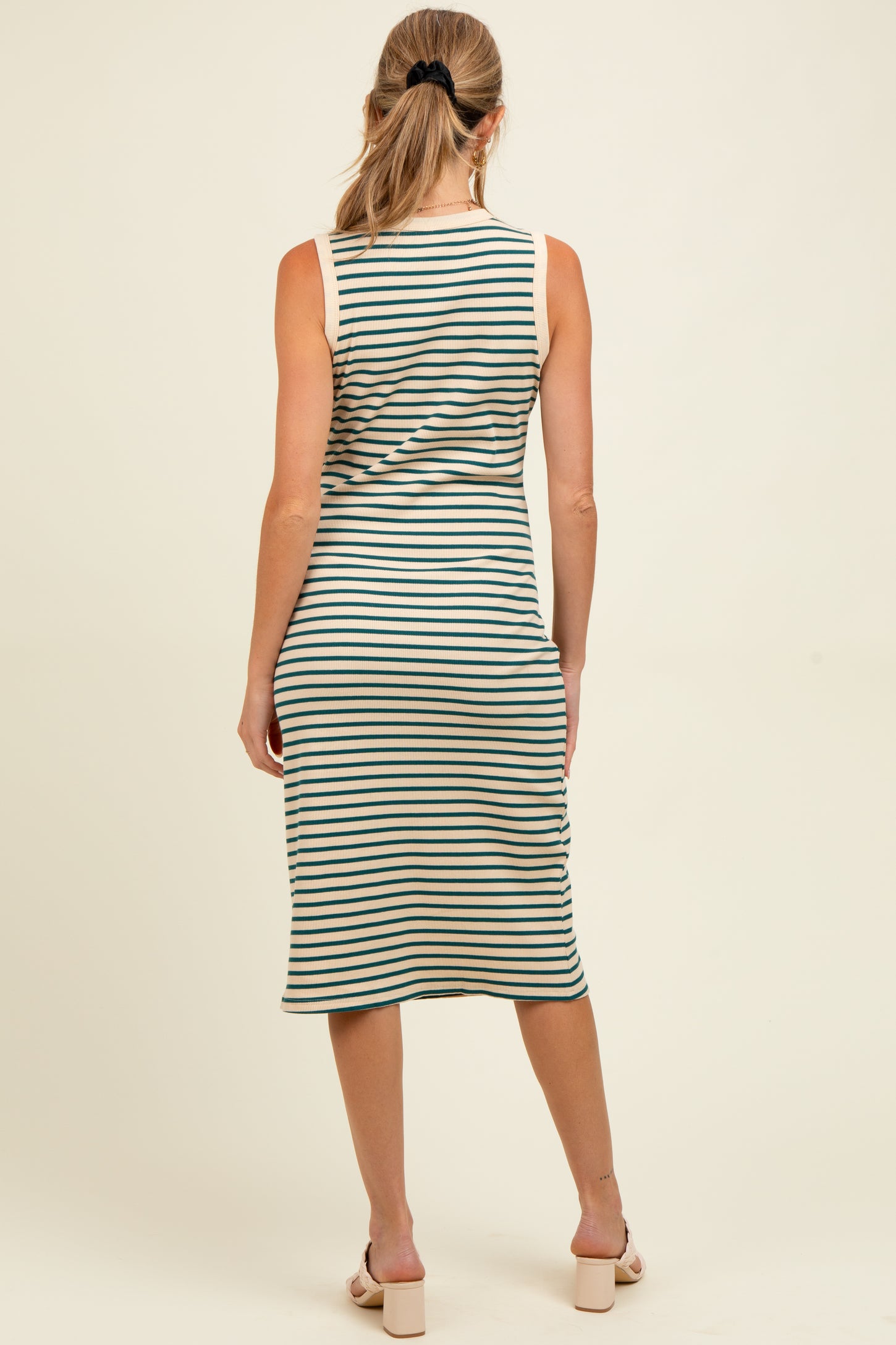 woman wearing a striped maternity midi dress with a fitted silhouette and sleeveless design, showing her baby bump