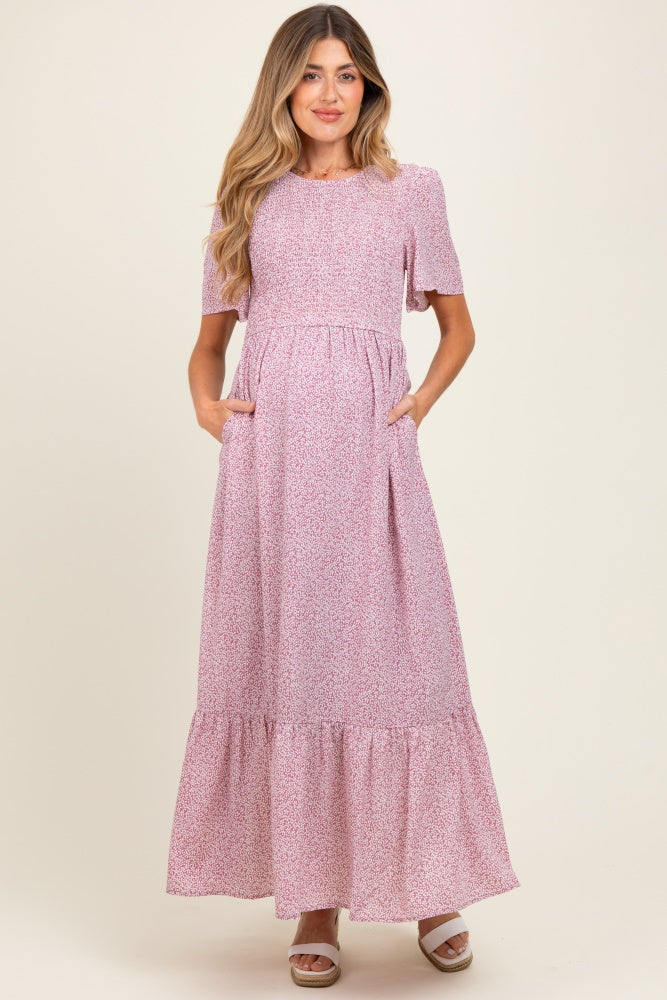 woman wearing a pink floral maternity maxi dress with short sleeves and pockets, showcasing her baby bump