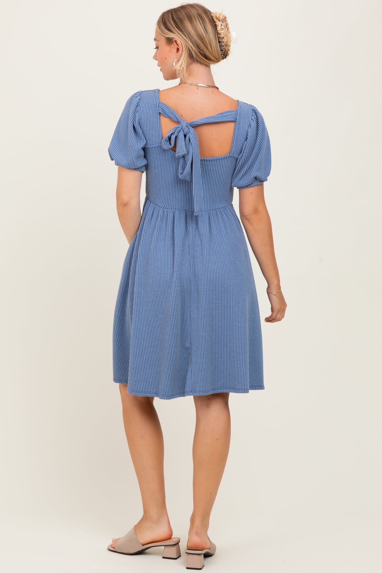 woman wearing a blue striped dress with puff sleeves and a tie-back detail, showing a fitted waist and flared skirt