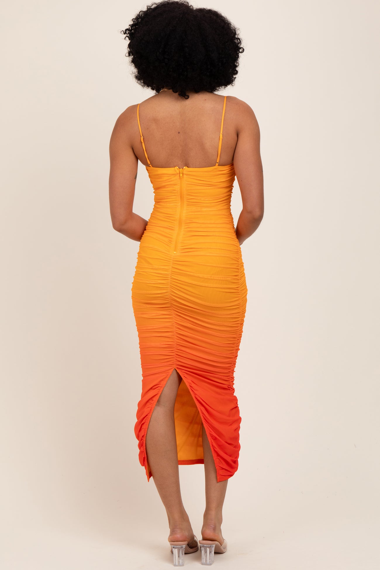 woman wearing a orange and yellow ombre bodycon dress with ruching and a side slit, viewed from the back