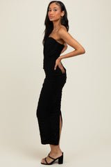 woman wearing a black strapless ruched midi dress with side slits and strappy heeled sandals