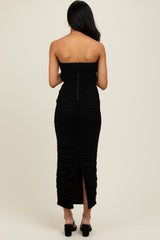 woman wearing a black strapless ruched midi dress with a back zipper and slit detail