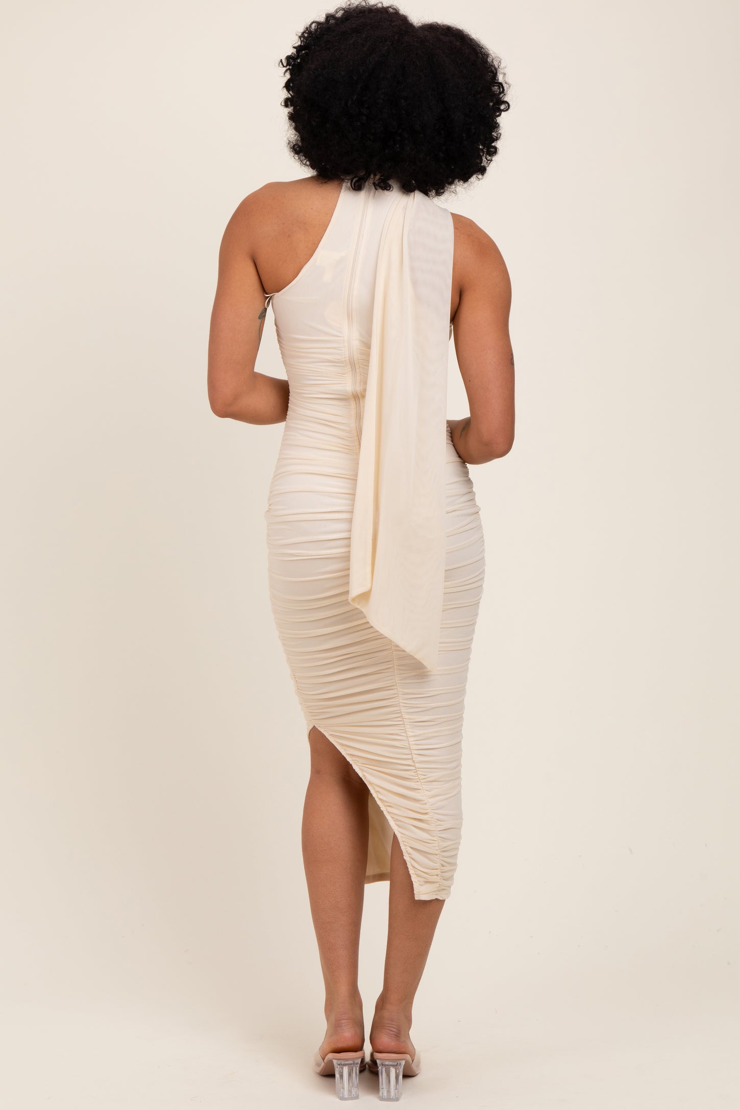 woman wearing a beige one-shoulder midi dress with ruching and a flowing drape at the back