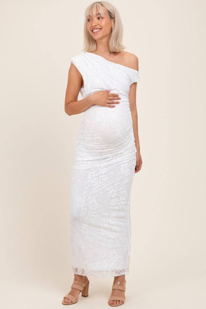 woman wearing a white one-shoulder lace maternity dress and holding her baby bump