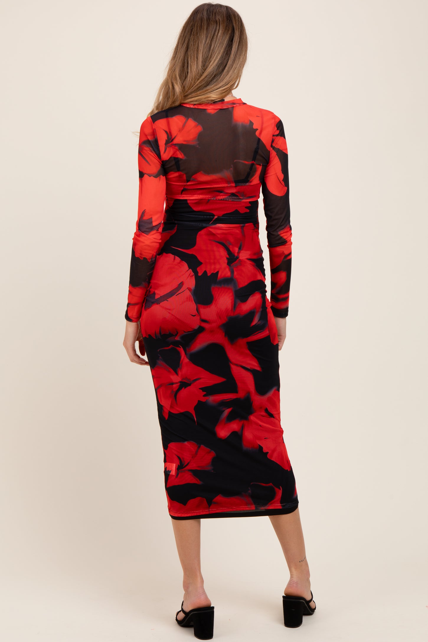 woman wearing a red floral print maternity dress with a fitted silhouette and long sleeves, showing her baby bump