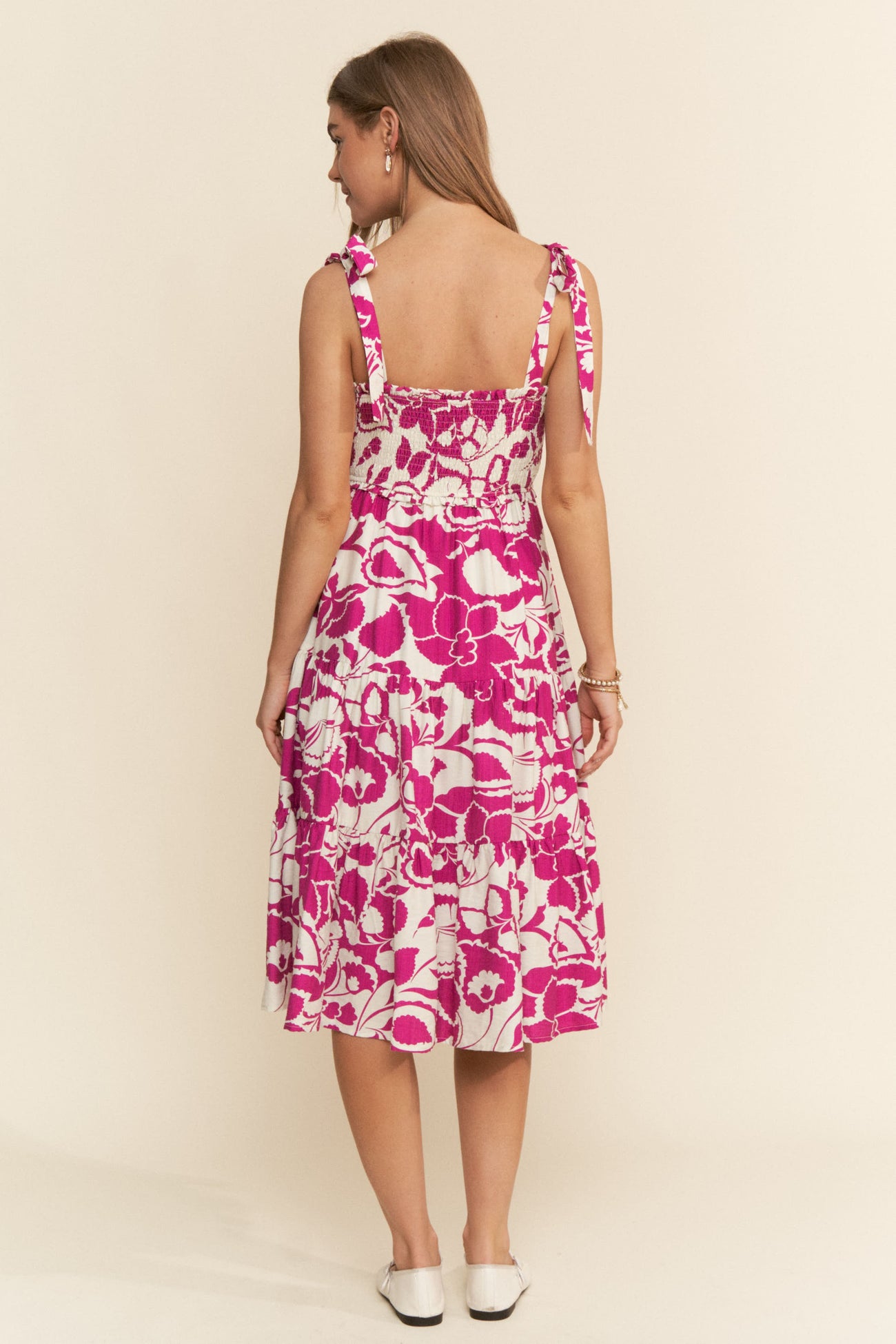 woman wearing a pink and white floral midi dress with tie straps and a smocked back, standing with her back to the camera