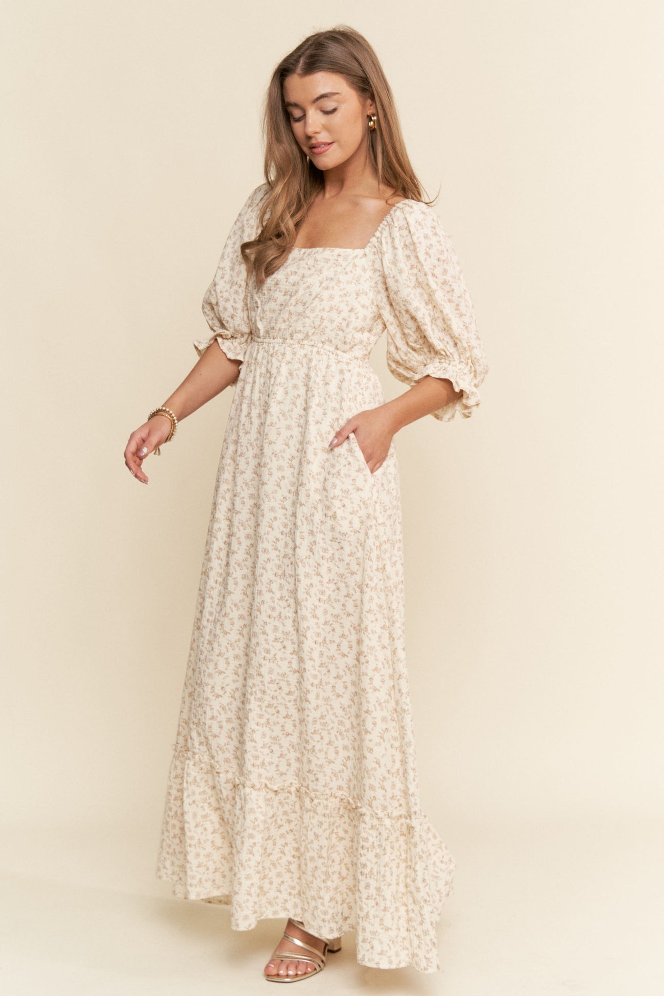 woman wearing a beige floral maxi dress with puffed sleeves and side pockets