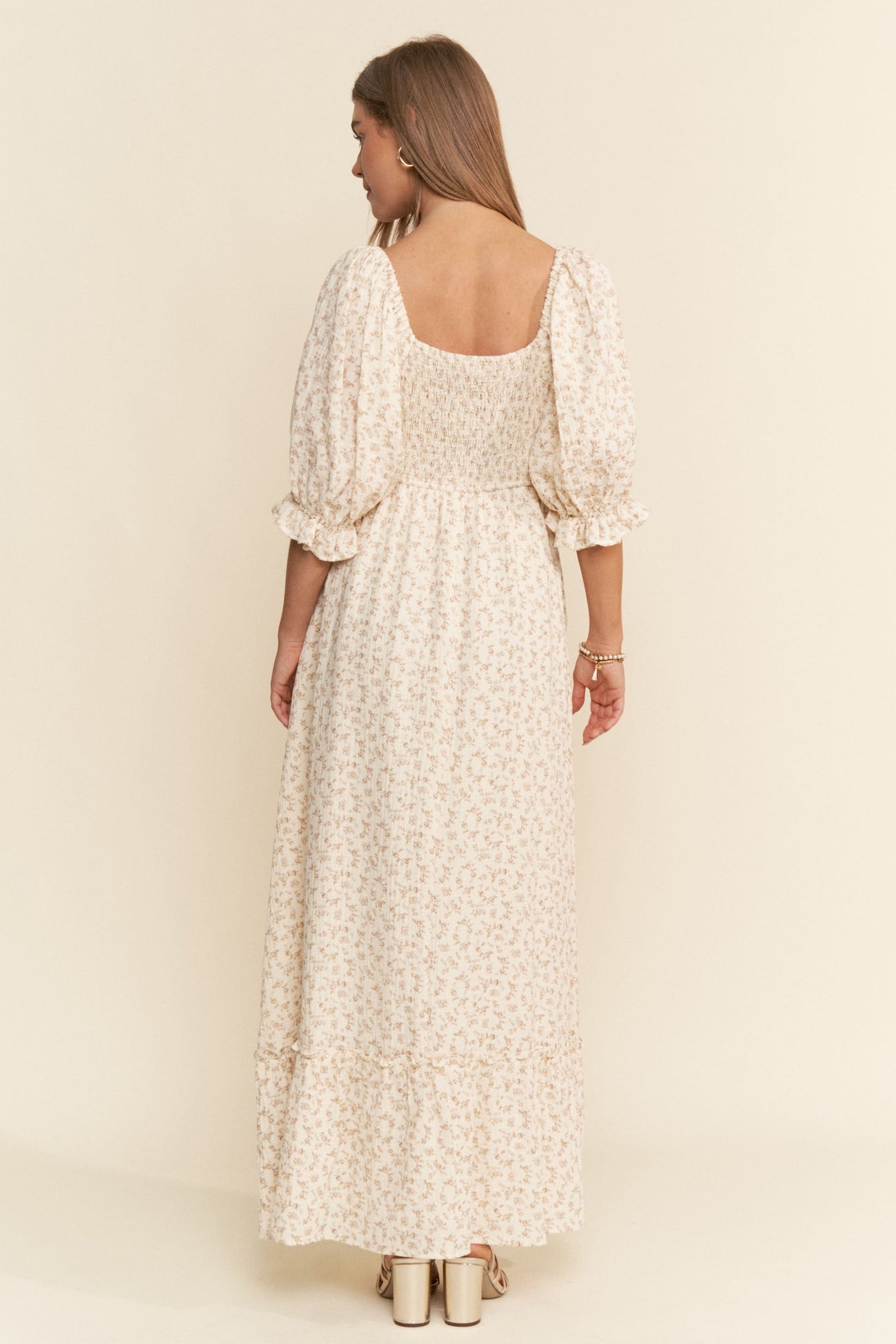 woman wearing a cream floral maxi dress with puff sleeves and a smocked bodice, shown from the back