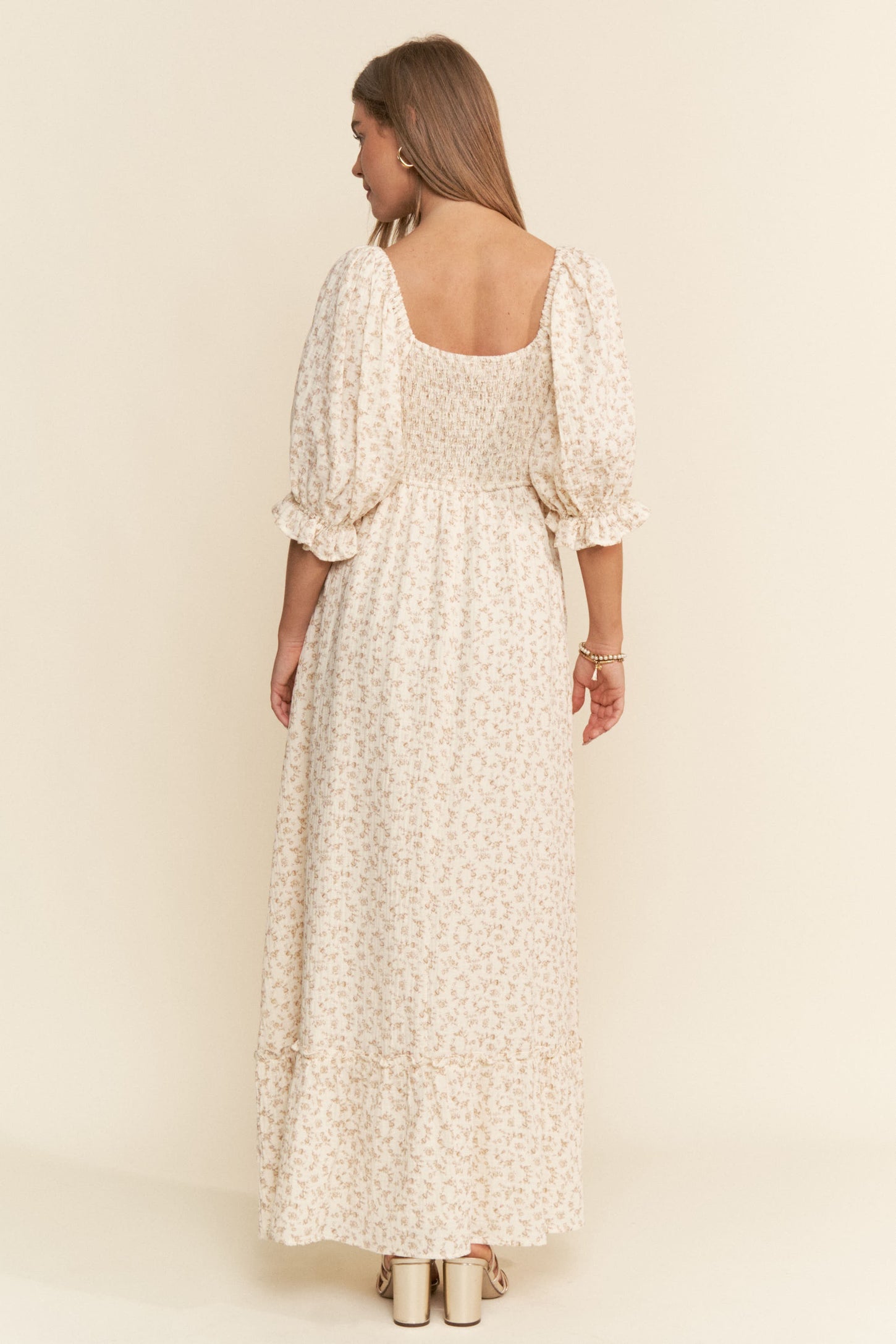 woman wearing a cream floral maxi dress with puff sleeves and a smocked bodice, shown from the back